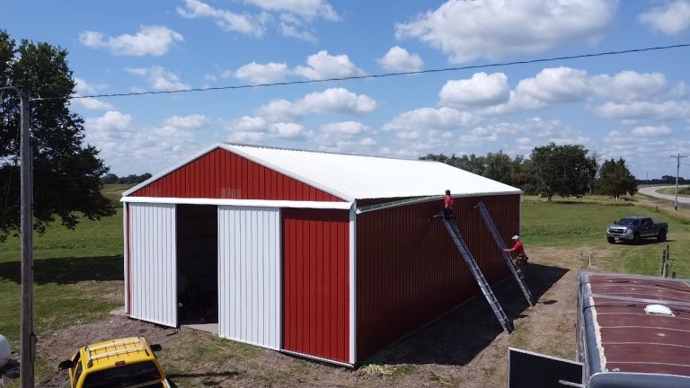 Red and white pole barn under construction in a rural area, featuring post-frame construction for cost-effective, versatile storage or workshop use.