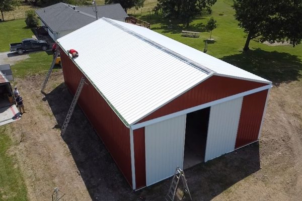 Red and white pole barn under construction in a rural area, featuring post-frame construction for cost-effective, versatile storage or workshop use.