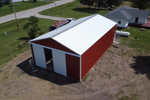 Red and white pole barn under construction in a rural area, featuring post-frame construction for cost-effective, versatile storage or workshop use.