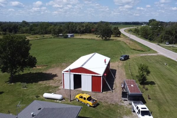 Red and white pole barn under construction in a rural area, featuring post-frame construction for cost-effective, versatile storage or workshop use.