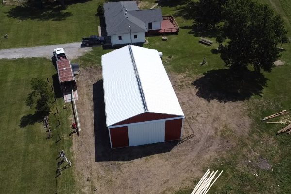 Red and white pole barn under construction in a rural area, featuring post-frame construction for cost-effective, versatile storage or workshop use.