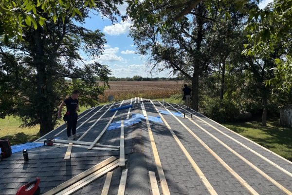 Roofing crew installing a metal roof overlay over asphalt shingles using furring strips to create a level surface and ventilation gap for the new metal panels.