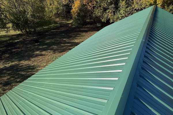 Newly installed green metal roof on a residential building featuring interlocking metal panels for long-lasting, energy-efficient performance.