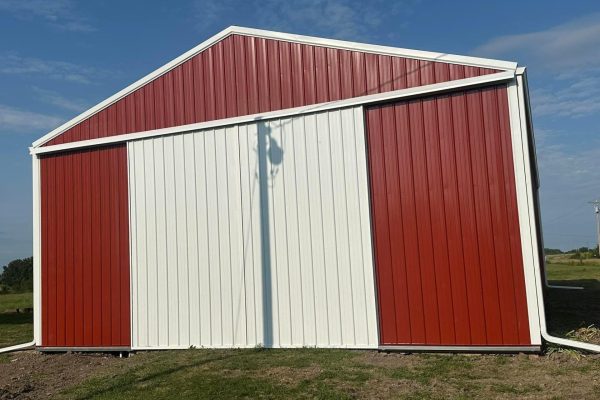 Red and white pole barn with large sliding doors and a white gutter system, built using post-frame construction for versatile agricultural or storage use.