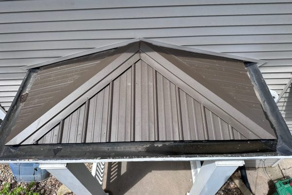 Small metal gable roof over an entrance with metal panels and decorative diagonal pieces, offering durable, low-maintenance weather protection.