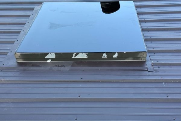 Metal roof with a skylight and round roof vent installed on corrugated panels, showing penetrations that require careful flashing to prevent leaks.